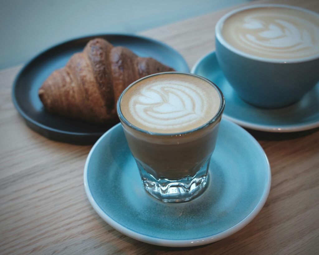 Two cups of coffee and a croissant on a table